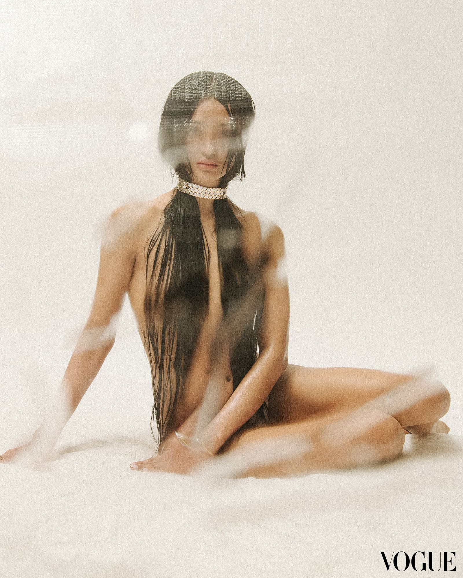 a woman sitting on the floor with long black wet hair wearing a metal cuff choker