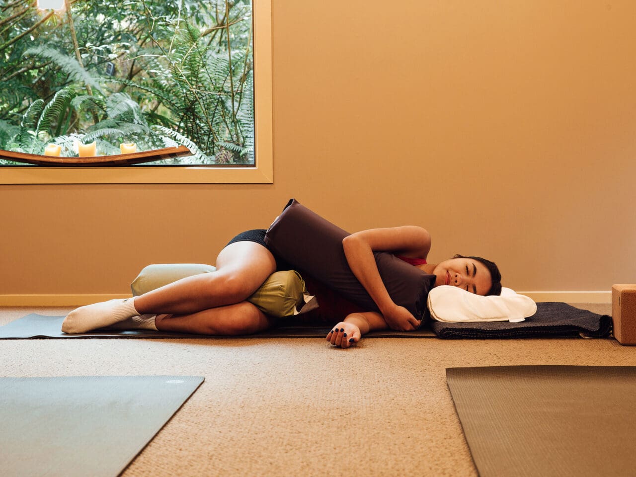 A woman laying down on a yoga mat and hugging pillows