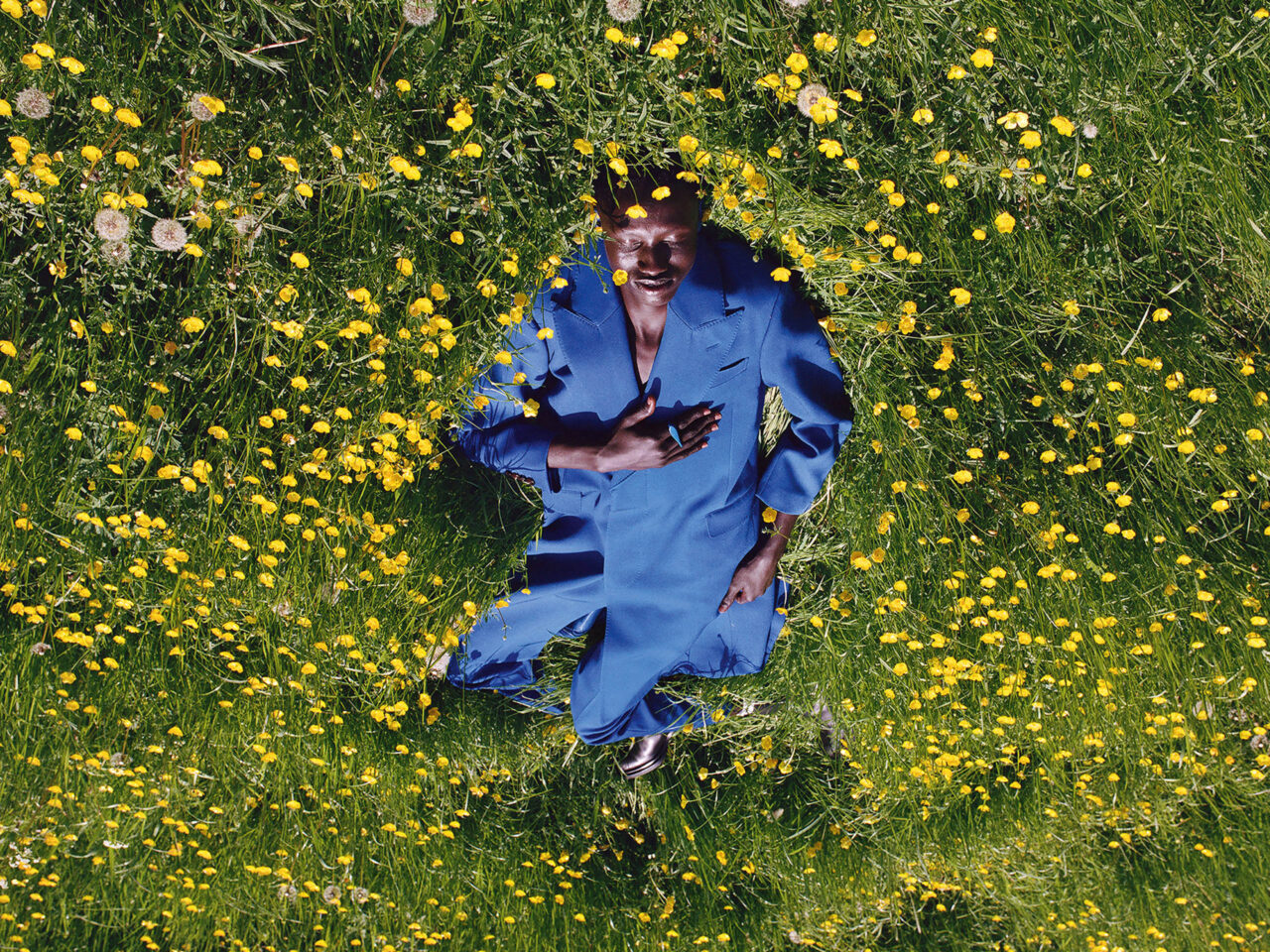 A model wearing a blue outfit on the green grass with yellow flowers