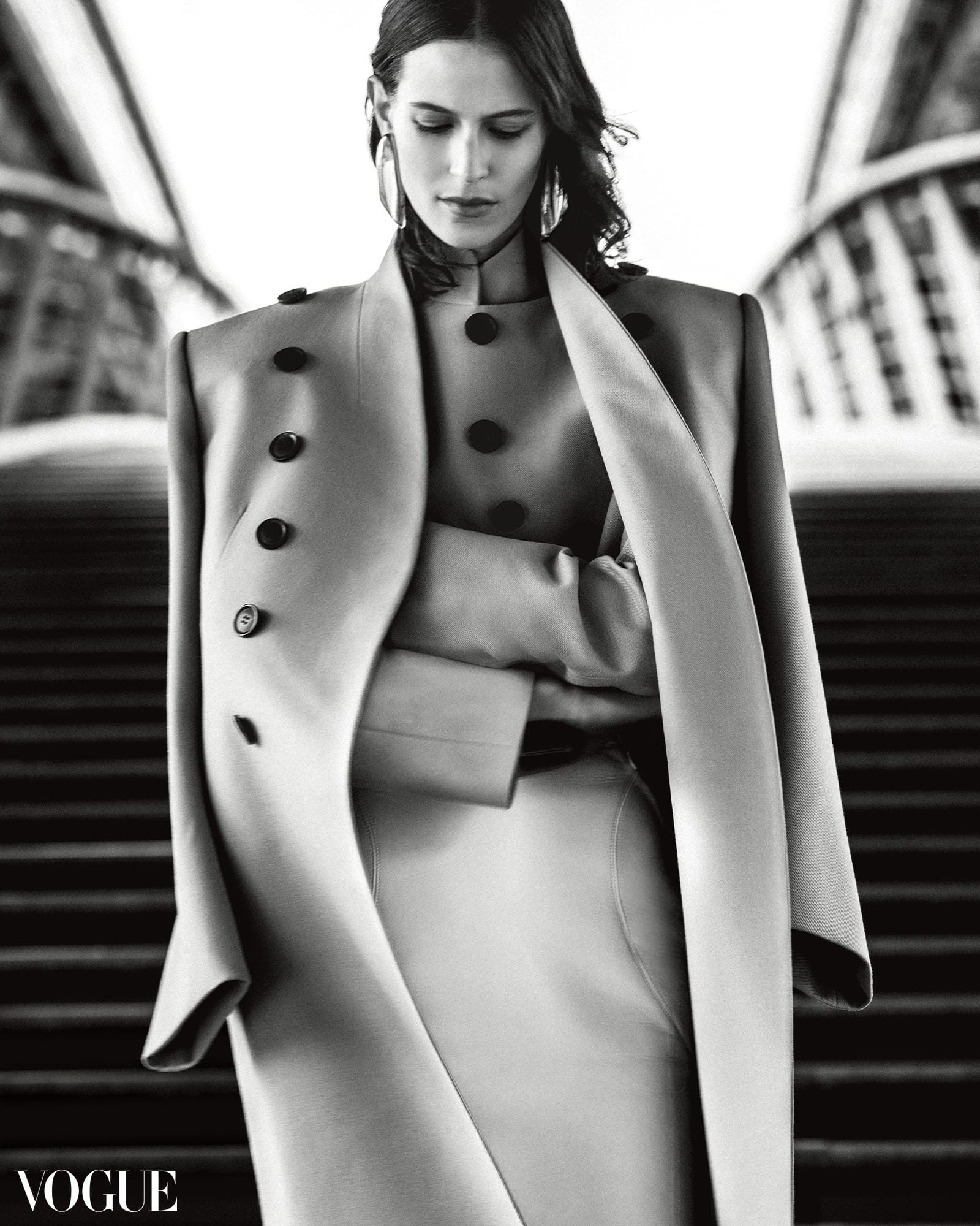Model Jeane Cadieu wearing an Alaïa coat, jacket, skirt, and earrings.