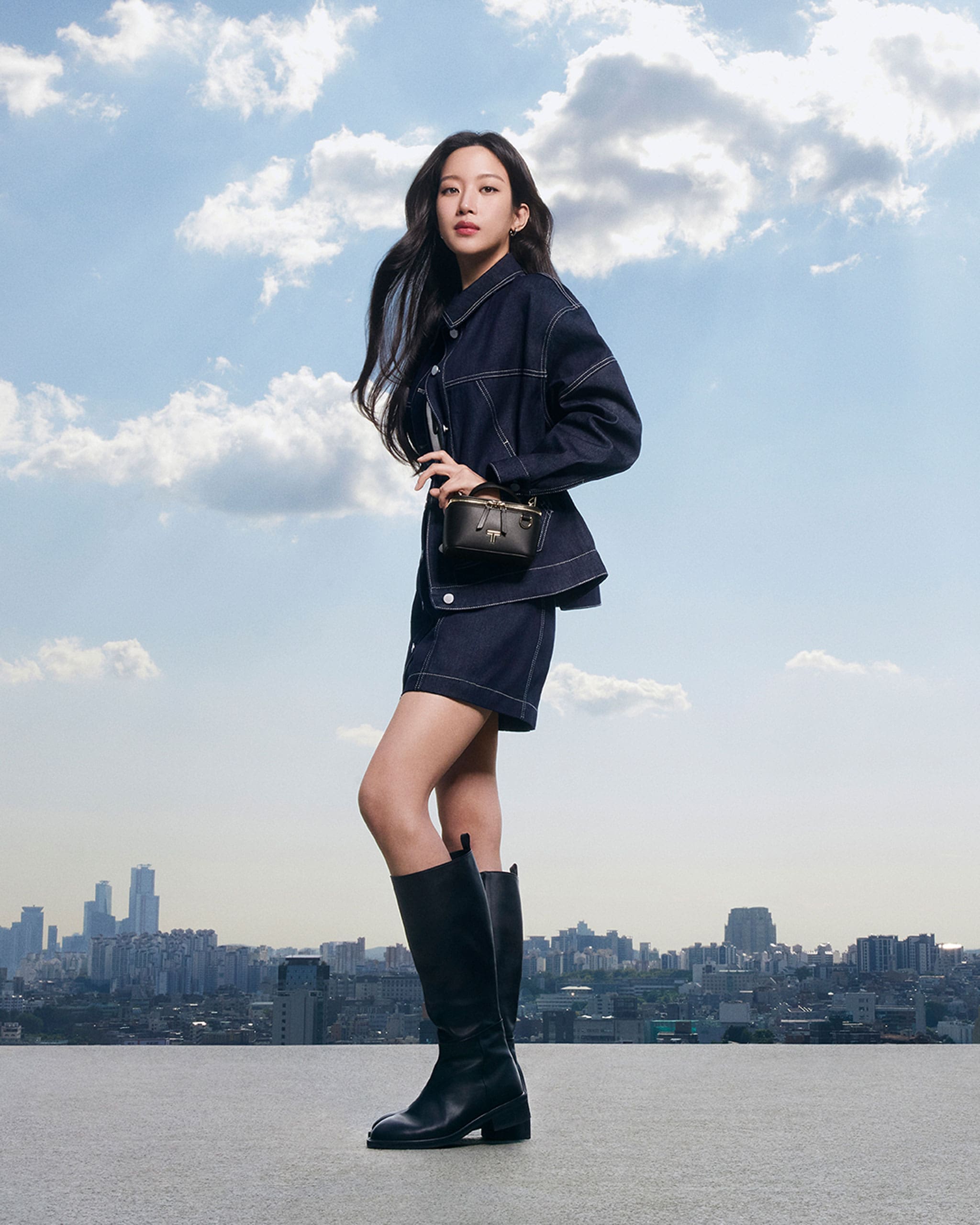 Mun Ka-Young wearing a denim jacket and denim shorts with knee-high boots and Lex Small Train Case crossbody from the TUMI Voyageur collection.