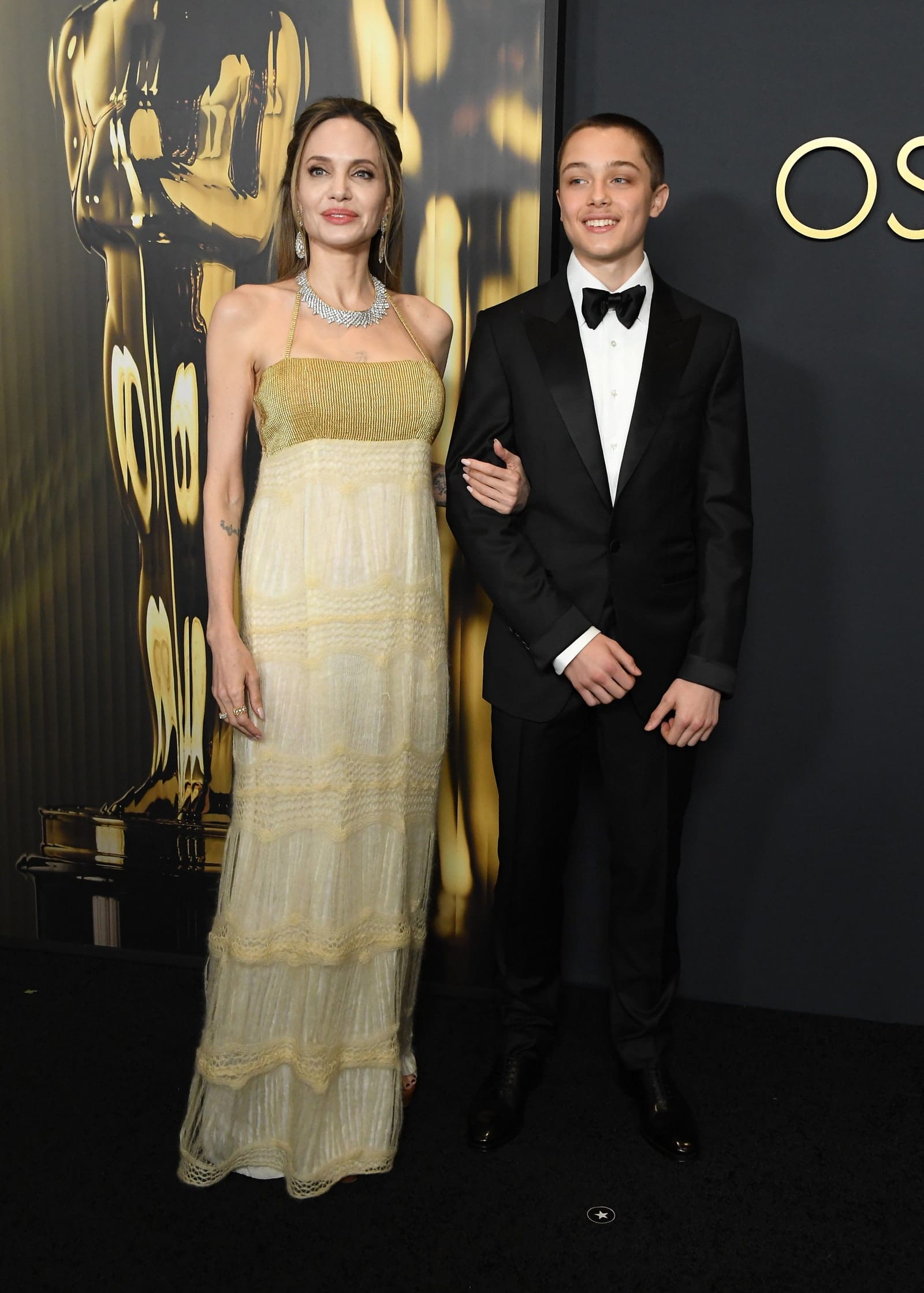 Angelina Jolie wears a gold halter neck dress with an empire waist that fell into a tiered lace off-white skirt, photographed with her son Knox.