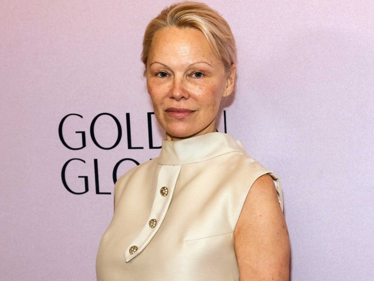 The Last Showgirl Actress Pamela Anderson wears a cream, silk a-line dress from the 60s, its buttoned up, rounded collar.