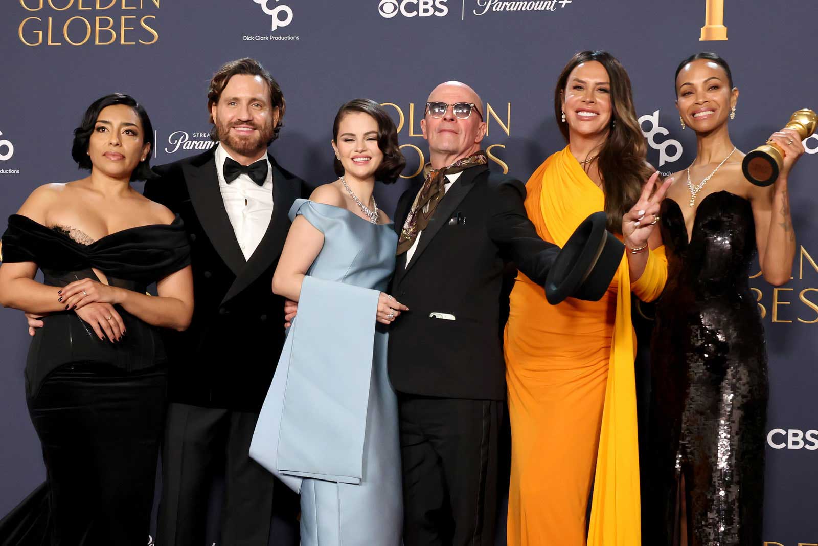 The cast of Emilia Perez including Adriana Paz, Edgar Ramírez, Selena Gomez, director Jacques Audiard, Karla Sofía Gascón, and Zoe Saldaña pose for a phoot at the Golden Globes.