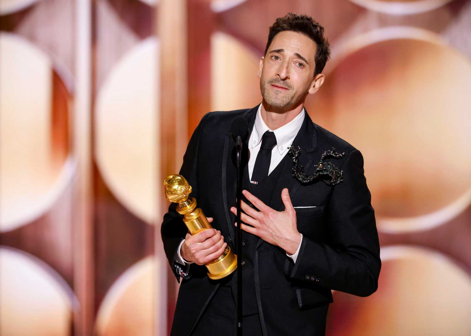 A photo of actor Adrien Brody holding his Golden Globe award, delivering a speech after winning for his role in 