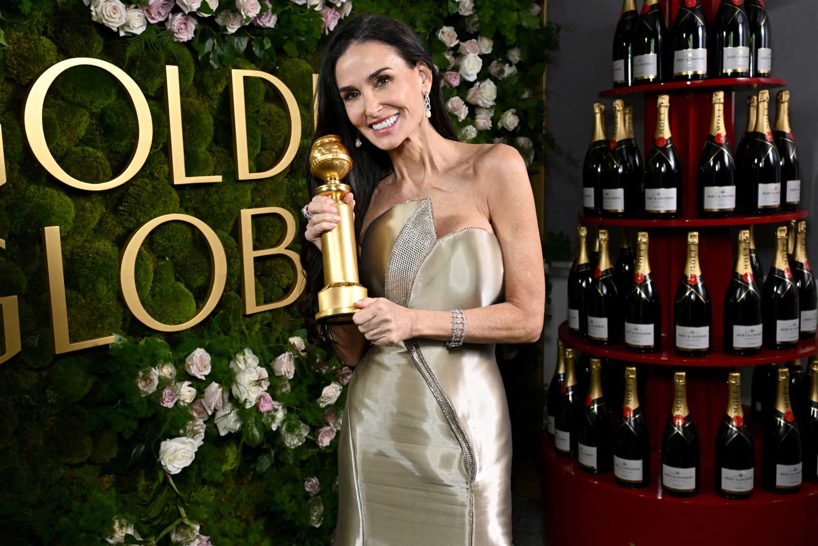 A photo of actress Demi Moore, posing in front of a Moet and Chandon tower, holding her Golden Globe award for her role in 