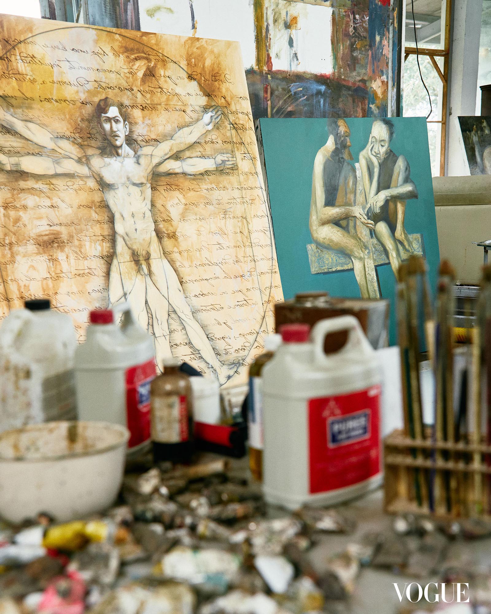 Photo of Manny Garibay's materials in the foreground, his paintings in the background.